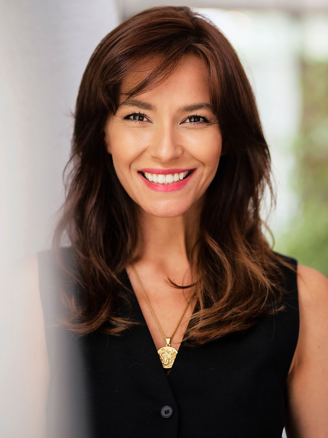 Smiling woman with long brown hair and necklace.